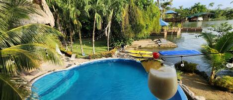 Zona de piscina con vista despejada al agua, rodeada de palmeras y una terraza de madera.