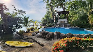 A pool surrounded by rocks and plants, with a yellow boat and a gazebo in the background.