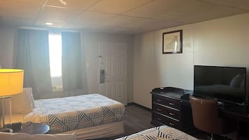 Une chambre d’hôtel avec deux lits, un bureau avec une télévision, une commode et une lampe.
