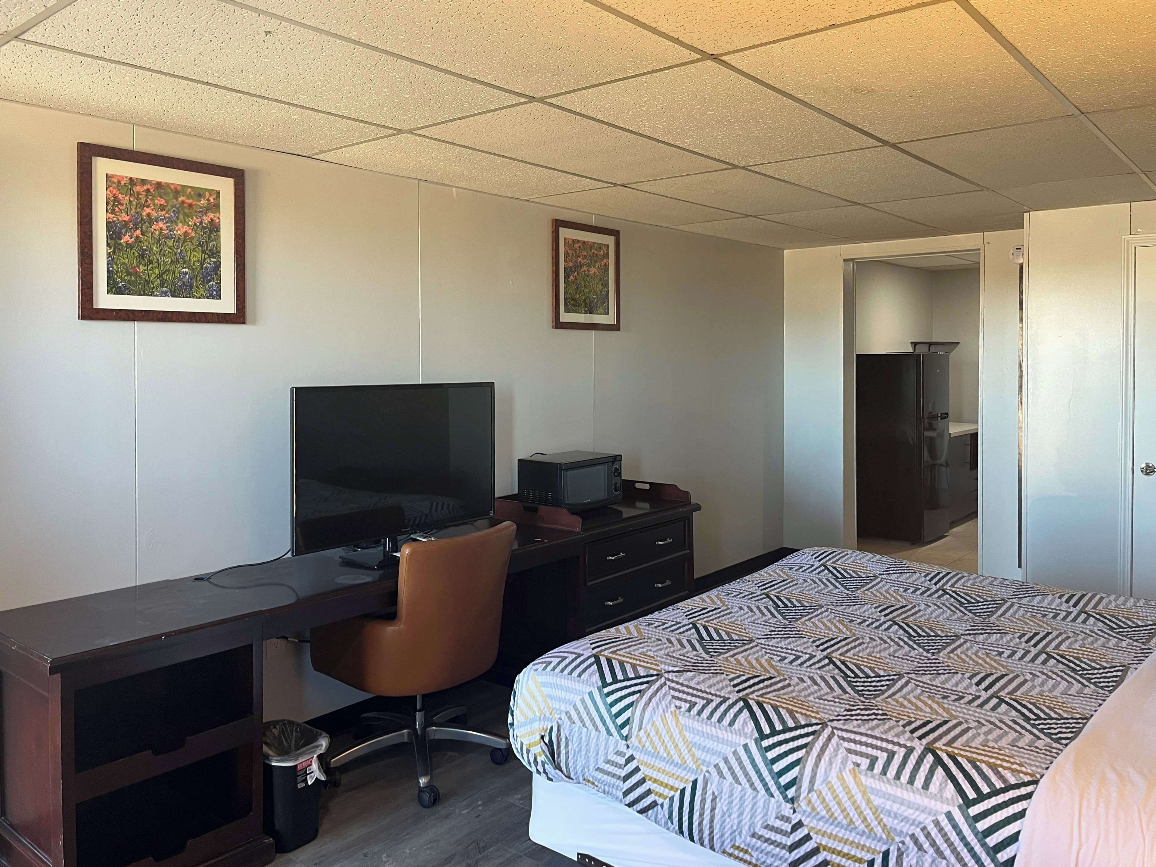 Habitación de hotel con cama, escritorio con computadora, silla, televisor, microondas y refrigerador.