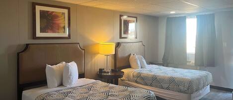 Une chambre d’hôtel avec deux lits, une table de chevet, une lampe et une fenêtre avec des rideaux.
