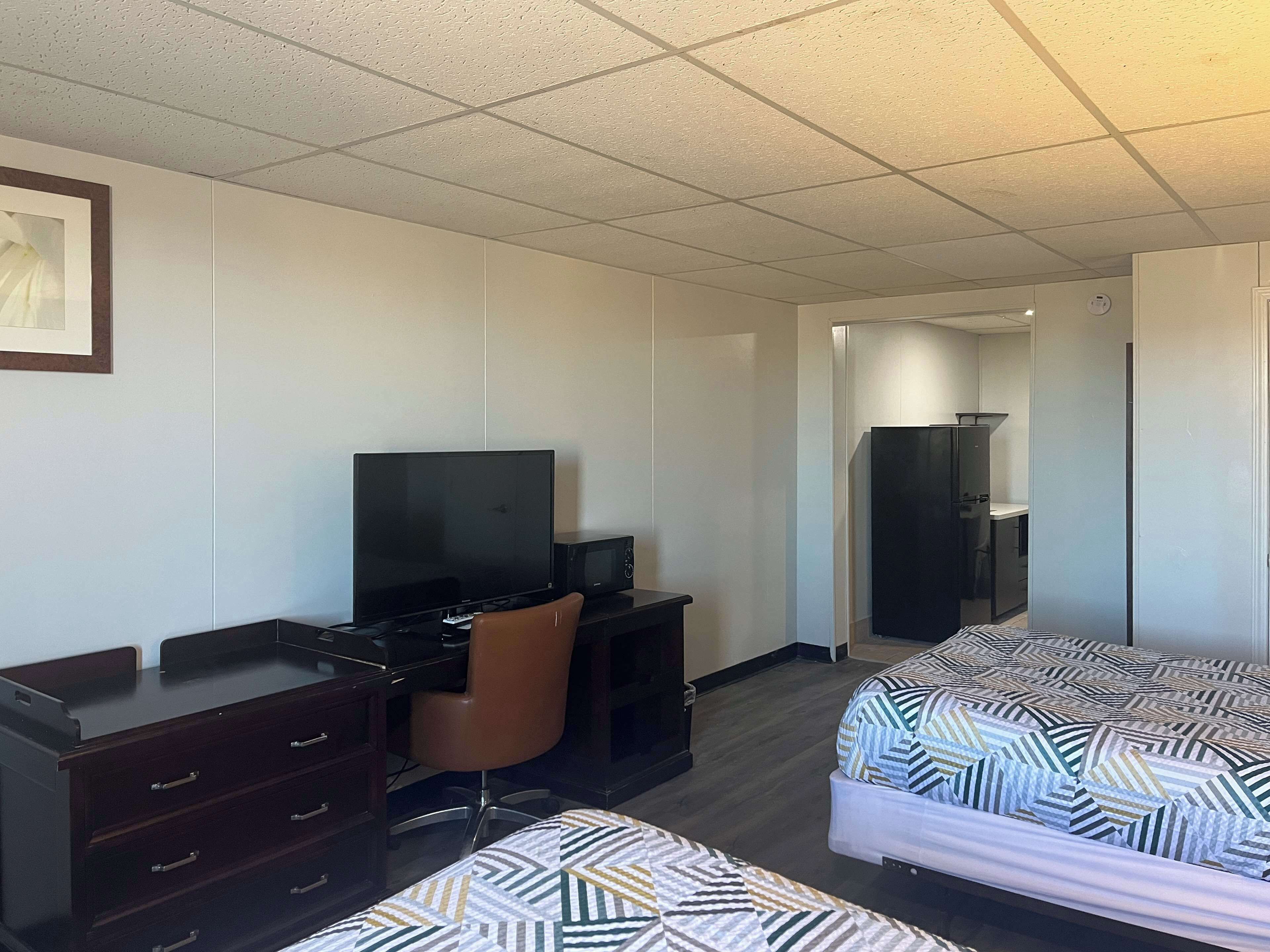 A hotel room with a desk, chair, television, wardrobe, and two beds.