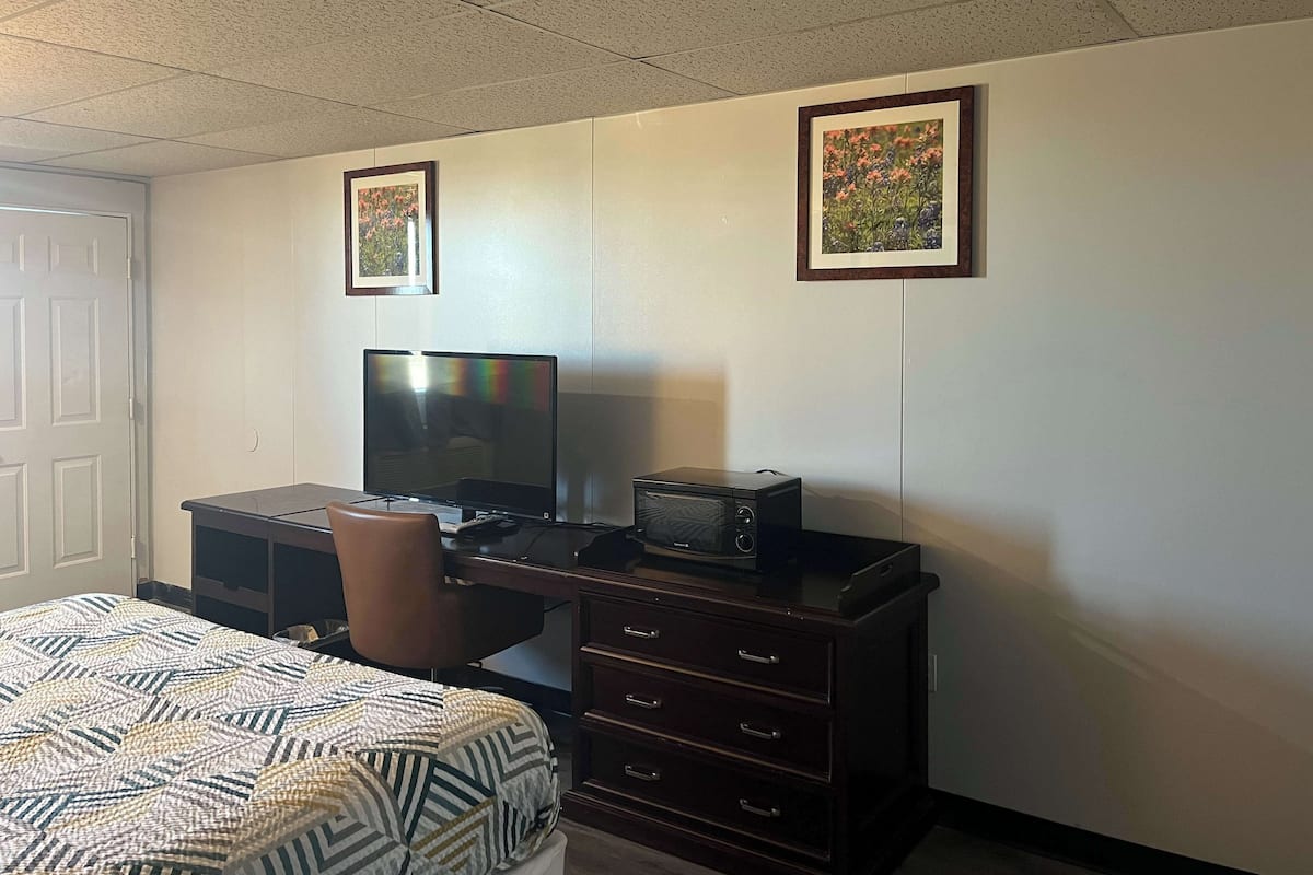 A hotel room with a bed, a desk with a television, a microwave, and two framed pictures on the wall.