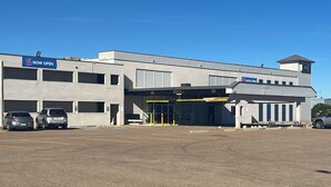 A commercial building with a 'NOW OPEN' sign, a parking lot, and a gated entrance.