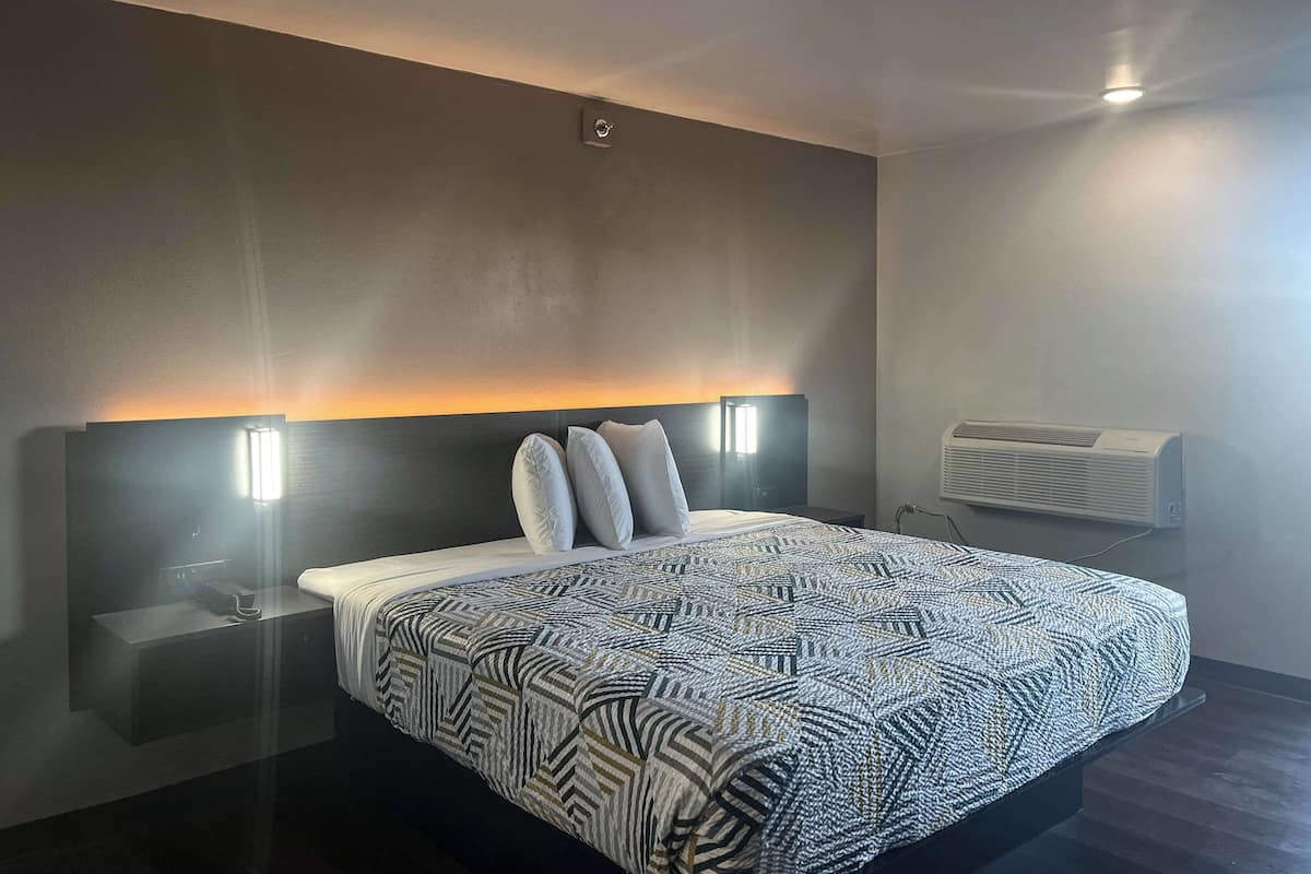 Una habitación de hotel moderna con una cama grande, una mesita de noche, aire acondicionado montado en la pared y una lámpara de techo.