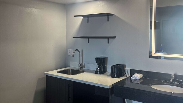 A compact bathroom with a sink, a mirror, a coffee maker, and a towel rack.