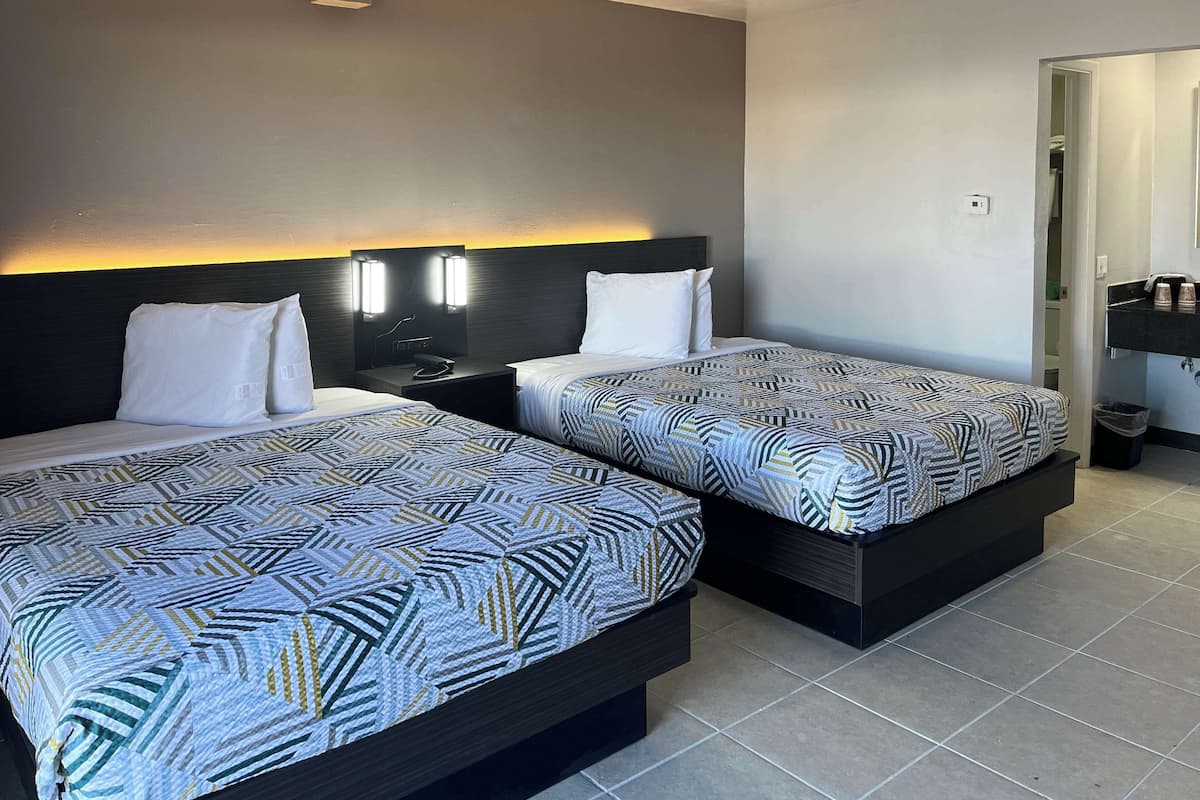 Habitación de hotel con dos camas, cada una con una colcha estampada, una mesita de noche con teléfono, y lámparas fijadas a la pared.