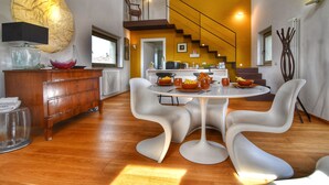 A modern kitchen with a central island, a dining area with white chairs, and a staircase leading to an upper level. - Design Loft Apartment (Marsciano)