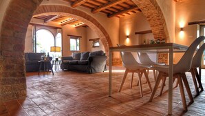 A rustic interior with exposed brick arches, a wooden ceiling, a dining table with chairs, and a sofa in a cozy living area. - Exclusive farmhouse with heated swimming pool (Marsciano)