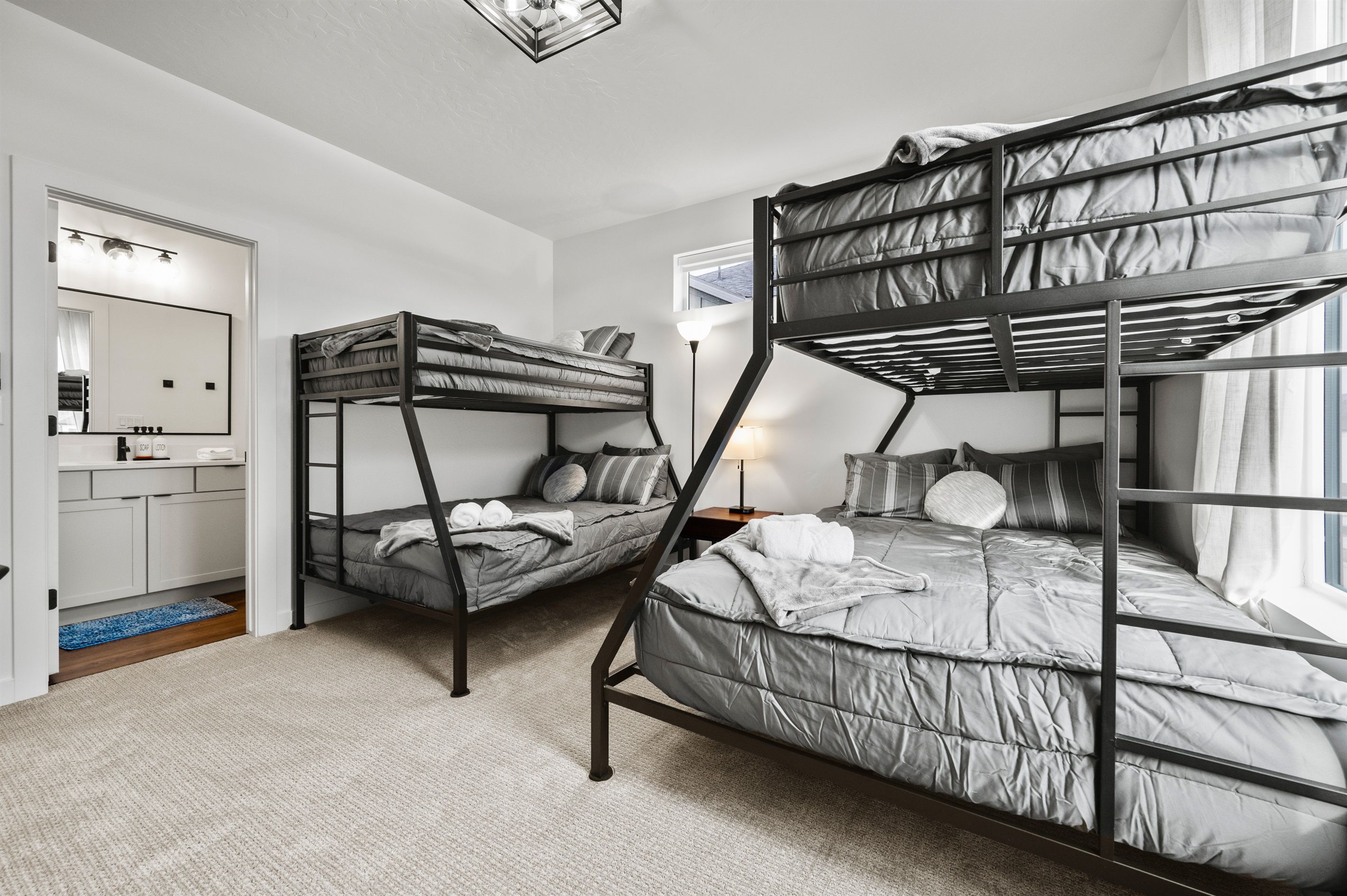 Een kamer met stapelbedden, een spiegel, een nachtkastje met een lamp en een raam met gordijnen.