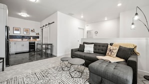 Una sala de estar moderna con un sofá gris, un tapete estampado y un comedor con una cocina al fondo.