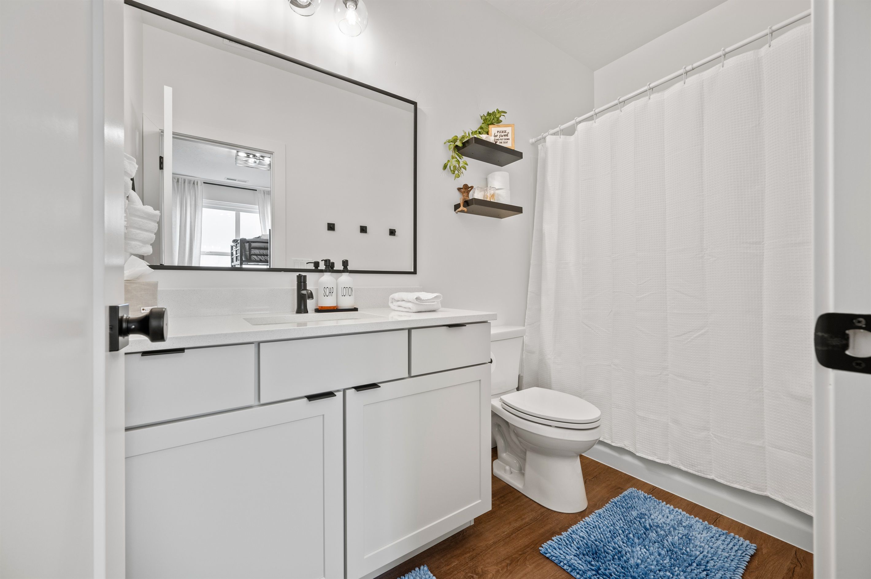 A modern bathroom with a white vanity, a large mirror, a toilet, and a shower curtain.