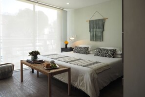 Une chambre moderne avec un grand lit, des tables de chevet, une lampe de chevet et une vue dégagée sur l’extérieur grâce à une grande fenêtre.