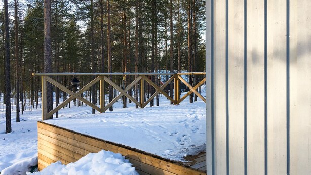 A wooden deck with a snow-covered ground, surrounded by tall pine trees. - Amazing apartment in Idre with sauna (Idre)