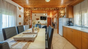 A dining area with a long table, chairs, and a wooden ceiling. There is a kitchen area with cabinets and a refrigerator. - Private Pool, Sunny Location, South Rethimno, Ideal for Adults (Saktouria)