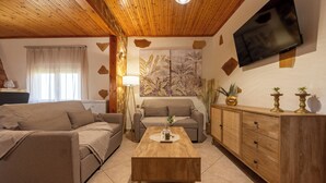 A living room with a wooden ceiling, a beige sofa, a wooden coffee table, a TV mounted on the wall, and a cabinet with decorative items. - Private Pool, Sunny Location, South Rethimno, Ideal for Adults (Saktouria)
