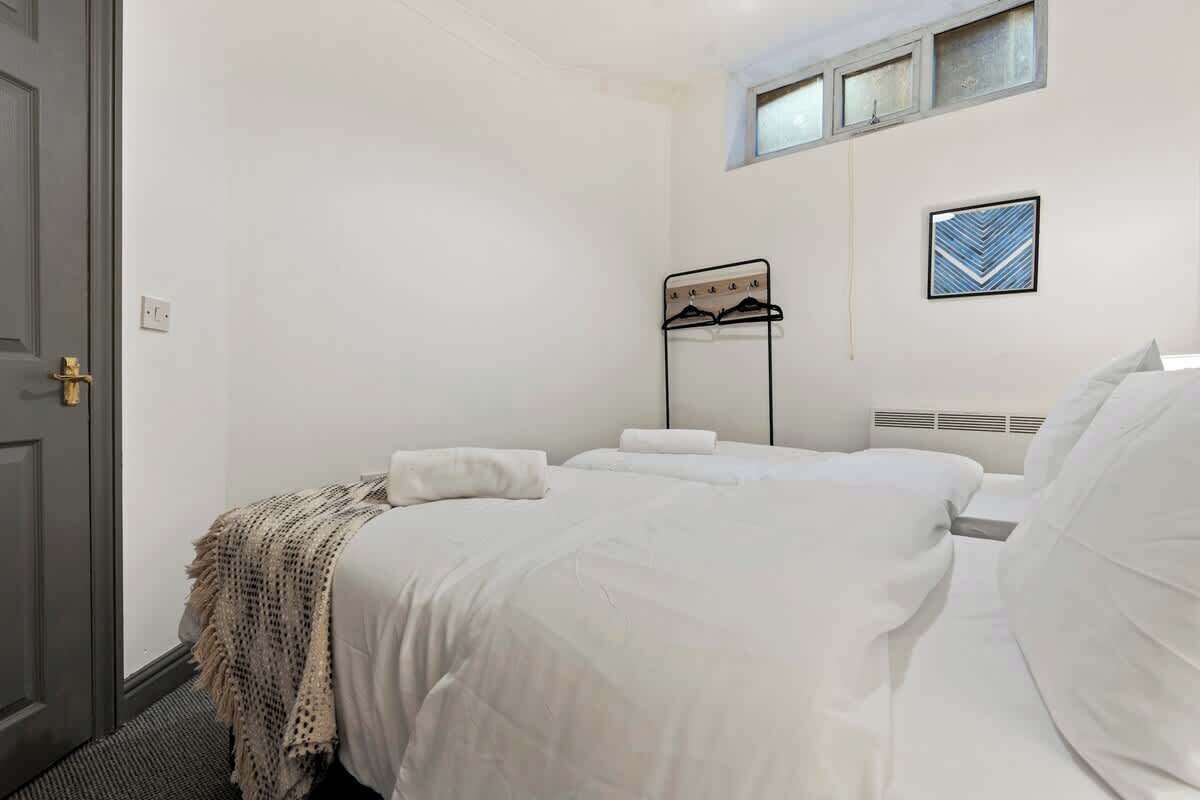 Une chambre à coucher avec un lit, un porte-manteau, une fenêtre et un tableau accroché au mur.
