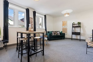 A modern living room with a green sofa, a coffee table, and a bar area with stools.