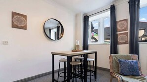 Ett rum med en rund spegel, ett litet bord med pallar, en stol med en kudde och två dekorativa föremål som hänger på väggen.