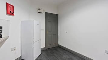 A hallway with a white refrigerator, a gray door, and a red fire safety sign on the wall.