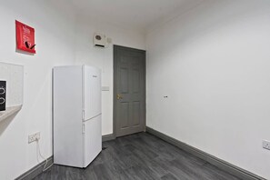A hallway with a white refrigerator, a gray door, and a red fire safety sign on the wall.