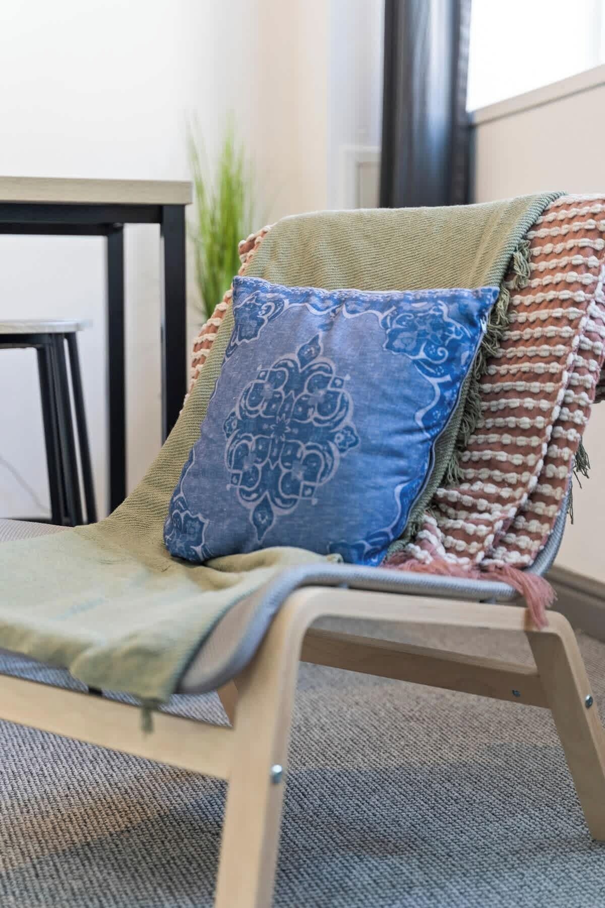 A chair with a green cushion and a blue patterned pillow, a woven blanket, and a metal frame.
