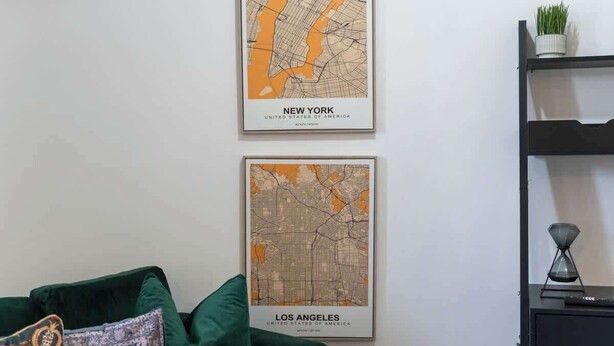 Två inramade stadskartor över New York och Los Angeles hänger på en vit vägg.