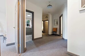 Un pasillo con piso alfombrado, una puerta que da a una cocina y una pequeña mesa con una silla.