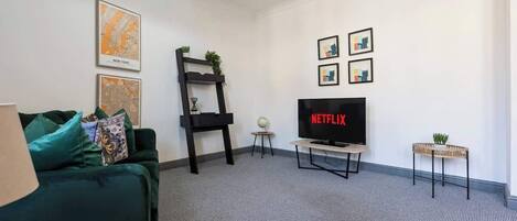 Een moderne woonkamer met een groene bank, een flatscreen televisie waarop 'NETFLIX' staat, een klein bijzettafeltje met een plant, en een wereldbol op een ander bijzettafeltje.