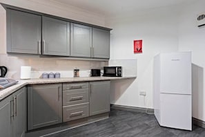 A compact kitchen with grey cabinets, a white refrigerator, a microwave, and a coffee maker.
