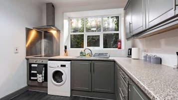 A compact kitchen with a built-in washer, a window with a view of greenery, and a stainless steel range hood.