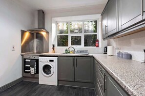 A compact kitchen with a built-in washer, a window with a view of greenery, and a stainless steel range hood. - Sienna's Apartment -2 Bed getaway in Pontypool (Pontypool)