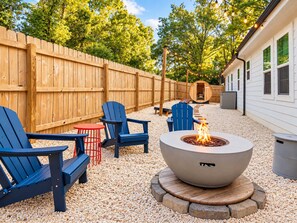 An outdoor seating area with Adirondack chairs, a fire pit, and a wooden deck. - Hot Tub & Sauna | Newly Renovated Outside (Charlotte)