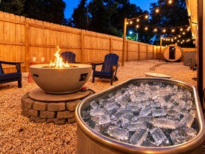 A fire pit with flames, surrounded by chairs and a cooler filled with ice. - Hot Tub & Sauna | Newly Renovated Outside (Charlotte)