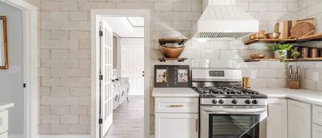 Una cocina con gabinetes blancos, estufa de acero inoxidable y salpicadero de ladrillo blanco.