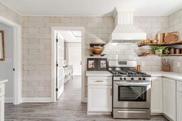 Una cocina con gabinetes blancos, estufa de acero inoxidable y salpicadero de ladrillo blanco.