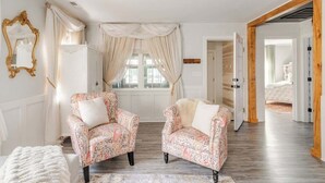 Una habitación con dos sillones estampados, un banco blanco y un ventanal con cortinas.