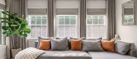A modern living room with a grey sectional sofa, a large potted plant, and a mirror on the wall.