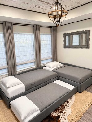 A modern bedroom with a sectional bed, large windows with curtains, a chandelier, and a mirror on the wall.