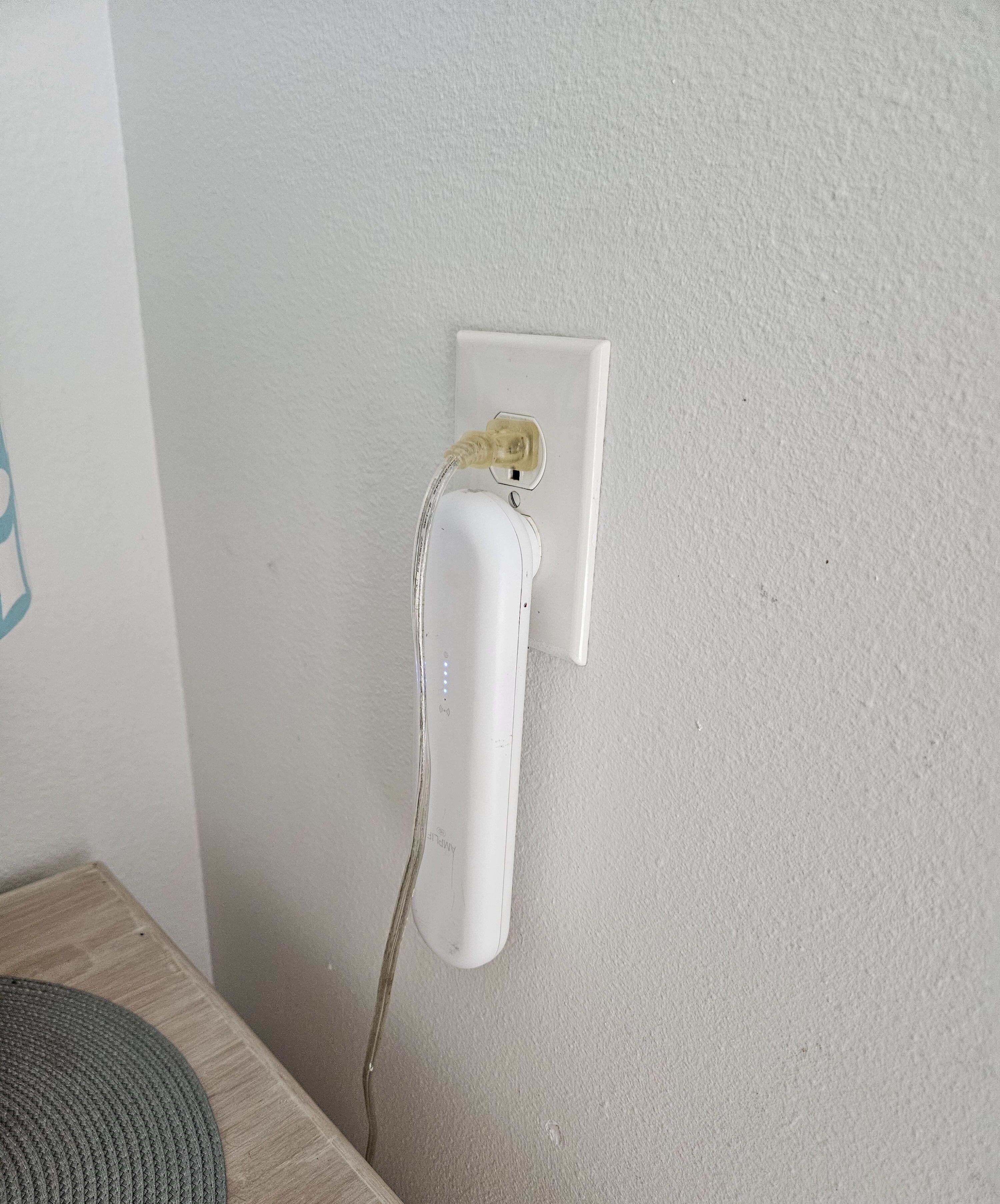 Eine weiße Wand mit einer Steckdose und einem angesteckten weißen Elektrogerät.
