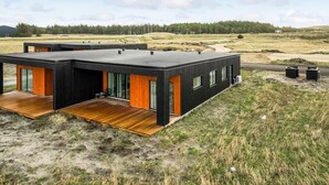 Una casa moderna de dos pisos con techo plano, ventanas amplias y una terraza de madera.