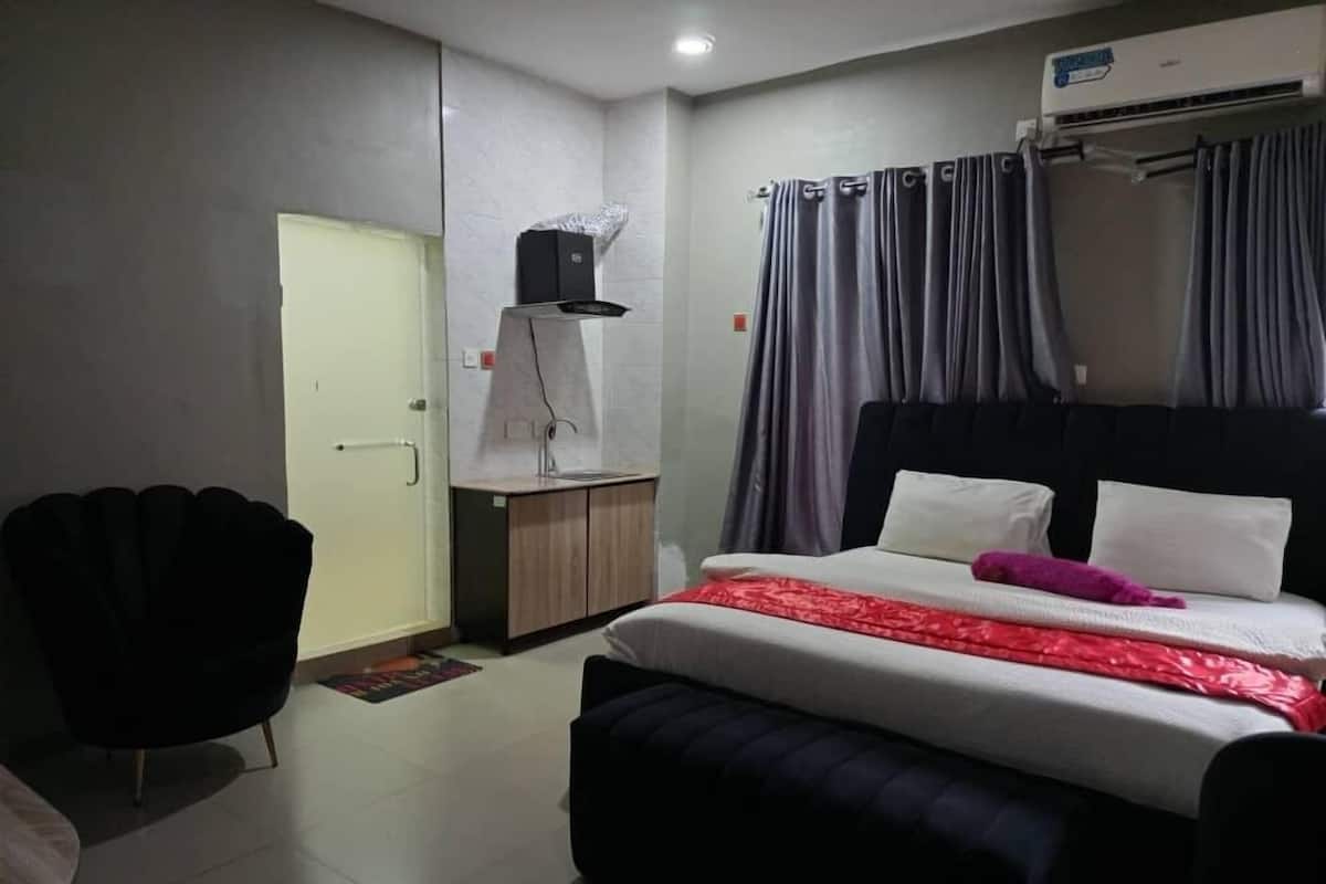 A hotel room with a bed, a desk, a chair, and an air conditioning unit.