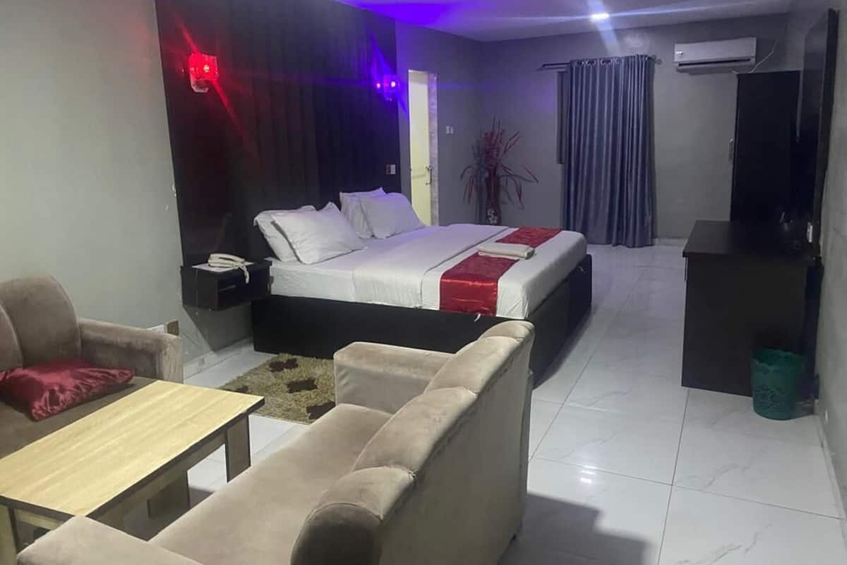 A hotel room with a bed, a sofa, a small table, a TV, and an air conditioning unit.