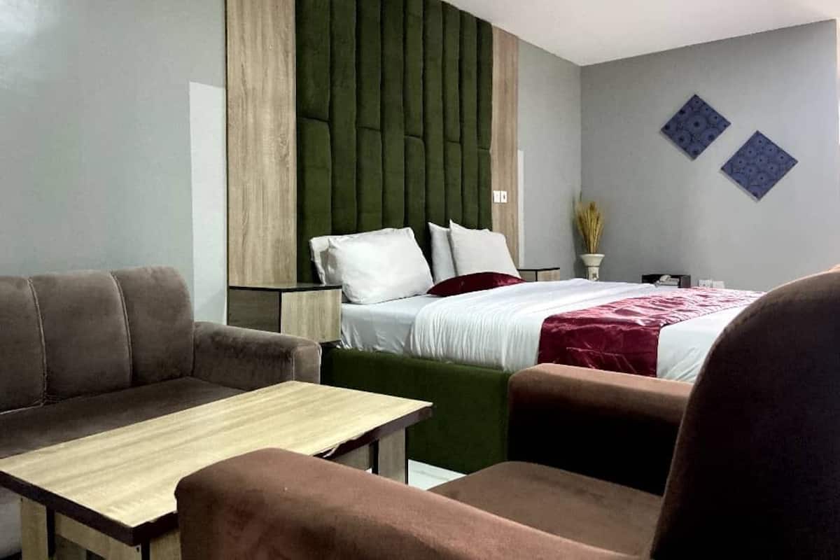 A modern hotel room with a bed, a sofa, a table, and a green accent wall.