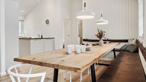 A modern kitchen with white cabinetry, a wooden dining table, and pendant lights.