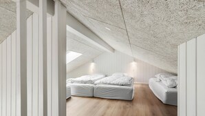 A bedroom with a sloped ceiling, wooden flooring, and two beds with white bedding.