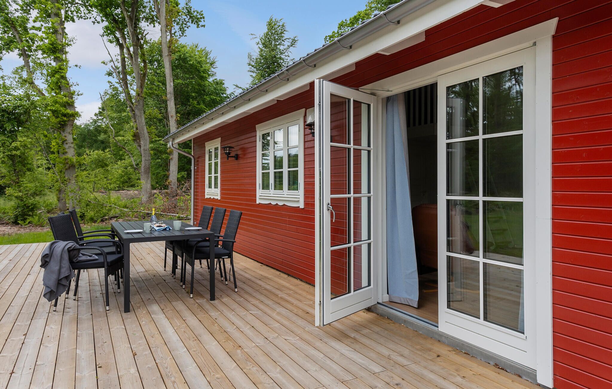 Eine rote Holzhütte mit einer Terrasse, einem Tisch und Stühlen sowie einer Glastür.