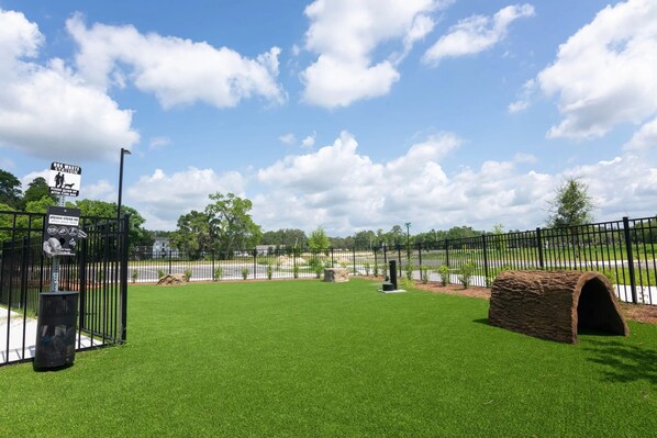 A fenced outdoor area with artificial grass, a stone structure, and a trash can.