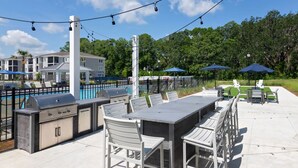 An outdoor patio with a barbecue grill, seating, and umbrellas.