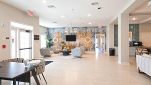 A spacious living area with a modern design, featuring a large flat-screen TV, comfortable seating, and a decorative wall with tropical leaf patterns.